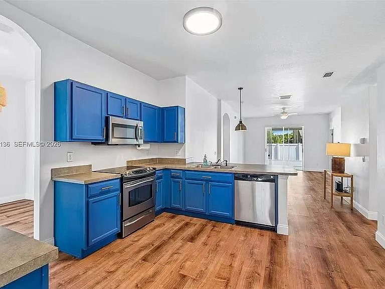 Open kitchen with blue cabinetry, breakfast bar, and stainless appliances, flowing into the main living area.