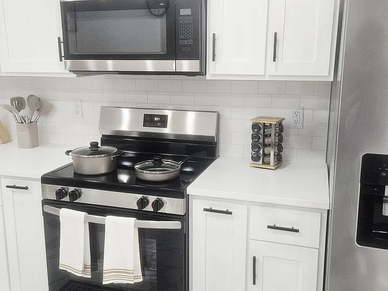 Kitchen features white shaker cabinetry, subway-tile backsplash, and stainless steel range with over-the-range microwave.