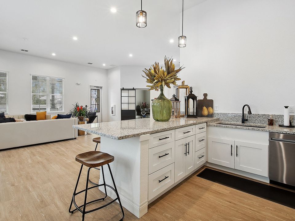 Chic open-concept kitchen and living area featuring elegant countertops, modern lighting, and cozy seating with vibrant cushions.