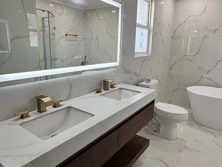 Spacious bathroom with dual-sink vanity, LED-lit mirror, and large-format marble-look tile for easy upkeep.