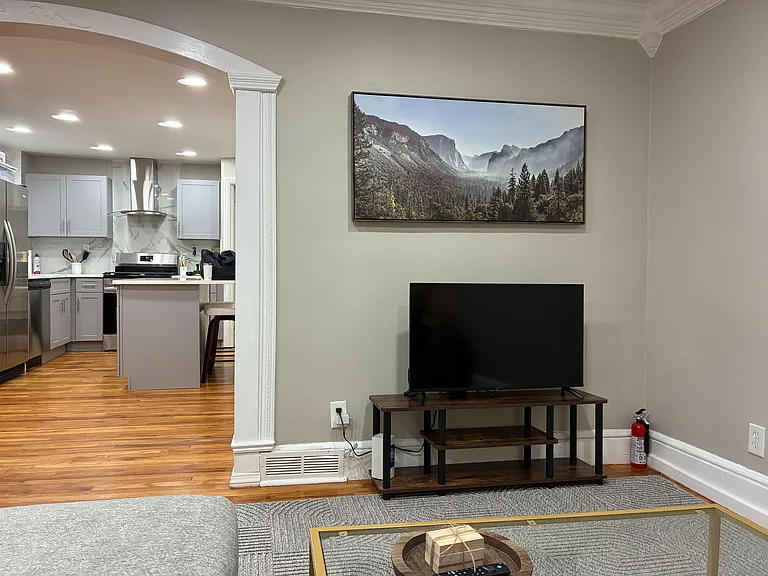 Shared living area with TV setup and easy flow into a well-equipped kitchen with bar seating and stainless appliances.