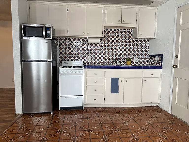 Kitchen includes artistic tile backsplash, refrigerator, stove/oven and microwave.