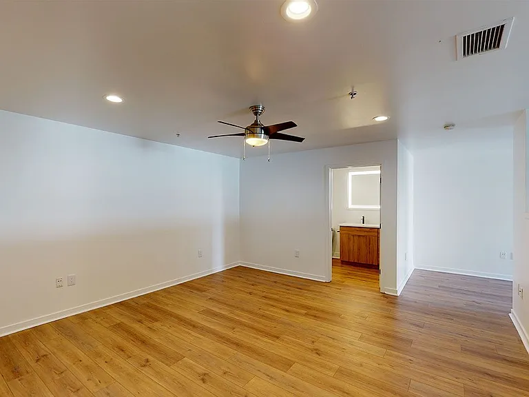 Spacious apartment bedroom with attached bathroom and wood-style flooring.