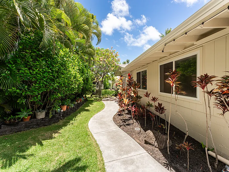 Landscaped side yard pathway lined with tropical greenery, offering a private and peaceful outdoor setting.