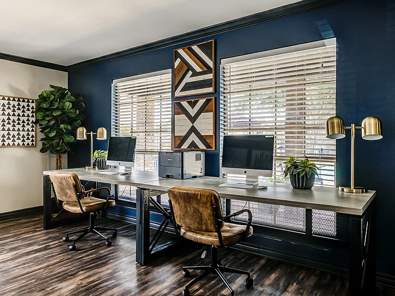 The business center of an apartment community is shown with two Apple desktop computers, leather chairs, and modern lighting.