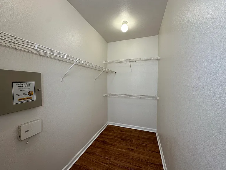 Spacious walk-in closet with sleek wire shelving and warm wood-style floors, ideal for organized storage. Spacious walk-in closet with sleek wire shelving and warm wood-style floors, ideal for organized storage.
