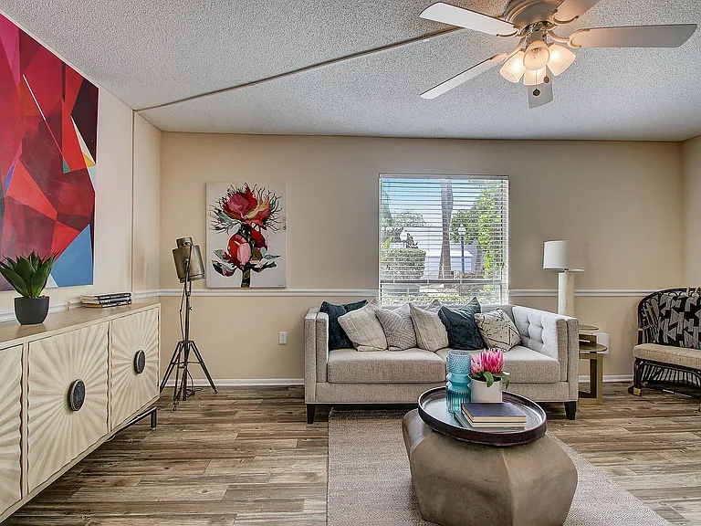 Charming living room with modern decor, featuring vibrant art, cozy sofa, and natural light from a large window.