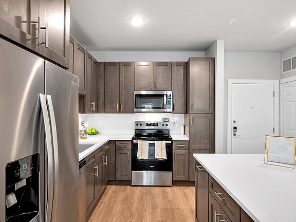 This thoughtfully designed kitchen offers a blend of sophistication and convenience. The dark wood cabinetry provides a refined touch, while the stainless steel appliances, including a refrigerator with a water dispenser, oven, and microwave, ensure moder