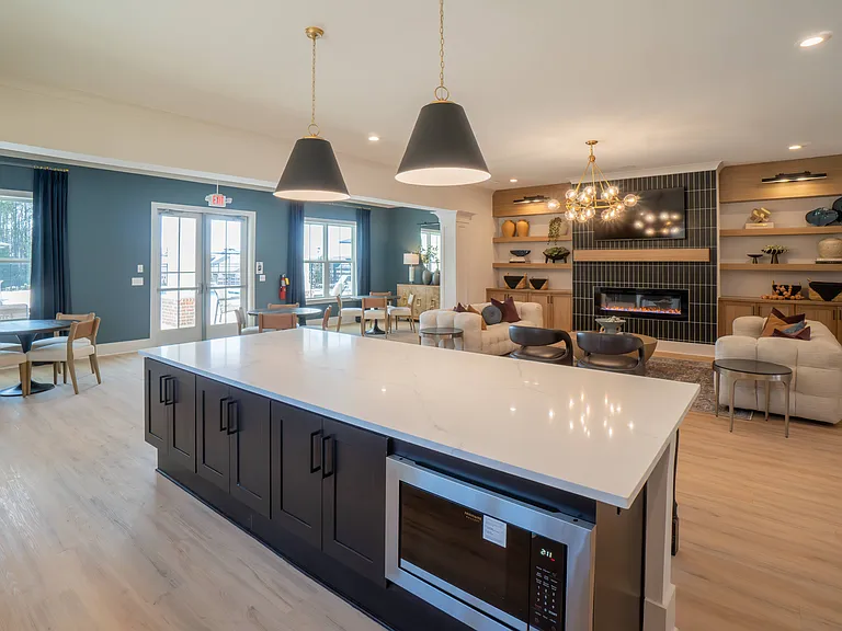 Kitchenette inside the Clubhouse with expansive island that offers bar seating and a microwave. Looking onto the living room area with ample seating, fireplace and TV.