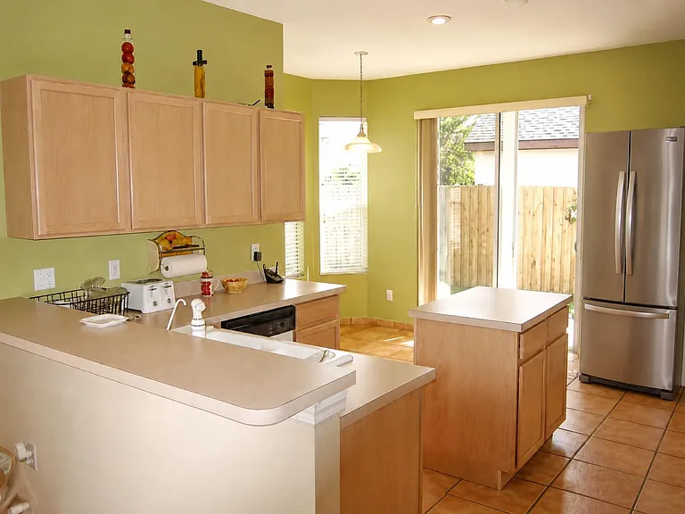 Spacious kitchen with ample cabinetry, center island workspace, and stainless refrigerator, plus patio access for easy dining