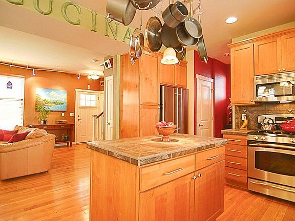 Kitchen has a great open layout and features light maple cabinets, tiled counters, gas range, all stainless appliances, center Island with hanging pot rack, and walk-in pantry.