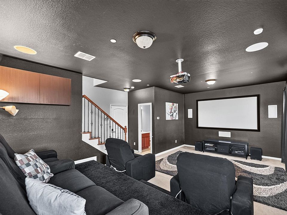 Home theater featuring a projection screen, tiered seating with black upholstered recliners, built-in media cabinetry, recessed and pendant lighting, and a finished basement with carpeted flooring and stair access to the main level