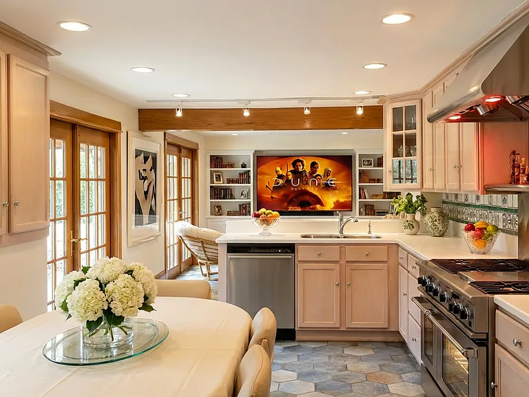"Bright, open kitchen with a large center island, Corian countertops, and stainless steel appliances, including a commercial-grade range. French doors bring in natural light and provide outdoor access. The kitchen is connected to a family room beyond.