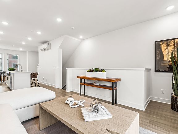 A modern and minimalist living room with a wooden coffee table, a white sofa, and a large potted pla