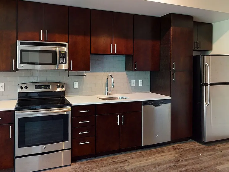 Apartment kitchen with stainless steel appliances, quartz countertops and wood-style flooring.