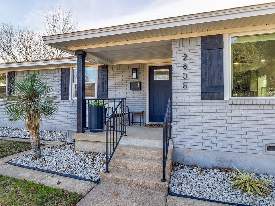 Light gray brick exterior featuring dark shutters, a covered porch with a black support column, and a dark entry door with a rectangular lite