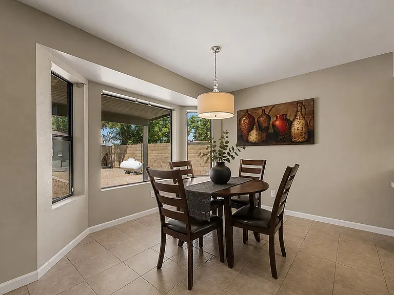Dining area features a four-seat table, tile flooring, and large windows with backyard views, plus a hanging light fixture.