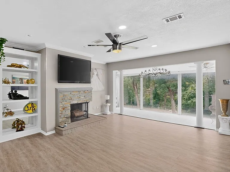 Bright living room with a fireplace and a ceiling fan, situated beside the sunroom; perfect for relaxation and comfort.