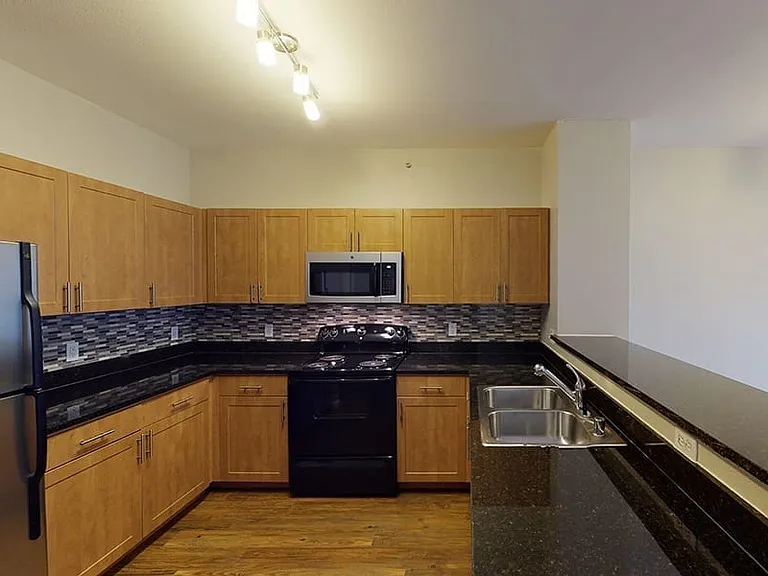 Apartment kitchen with granite countertops and wood-style flooring.