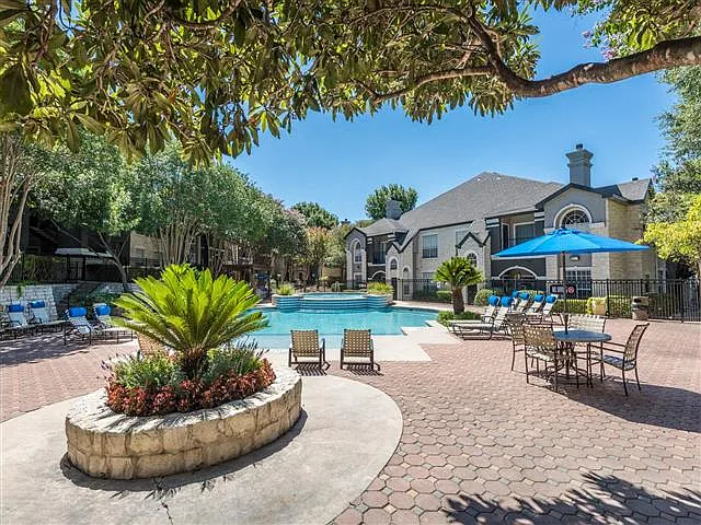 Community pool with umbrella covered table seating surrounded by shade trees