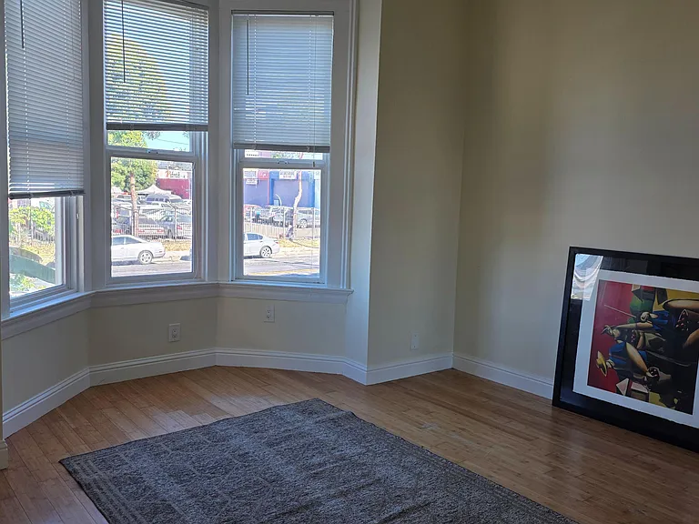 Spacious room with a bay window and hardwood floors, offering ample wall space and natural light for flexible furnishing.