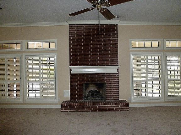 Focal point of the  oversize living area is this pretty brick fireplace surrounded by windows w/ plantation shutters, overlooking beautiful patio and treed backyard
