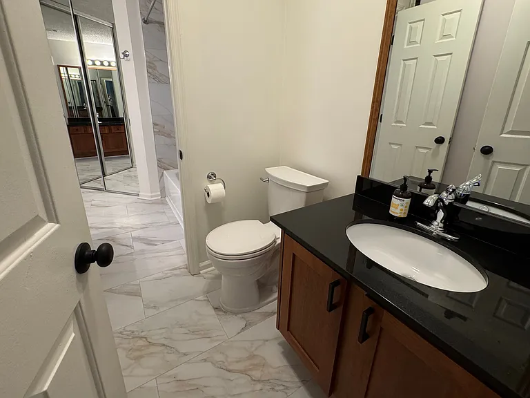 toilet with second sink and doorway into the large bathroom and walk-in closet