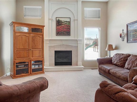 The great room features a floor to ceiling fire place, large windows, and ceiling fan.