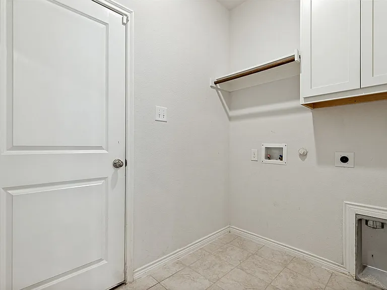 Dedicated utility space featuring a white paneled door, light-toned tile flooring, built-in white cabinetry, a floating shelf with a hanging rod, and appliance hookups