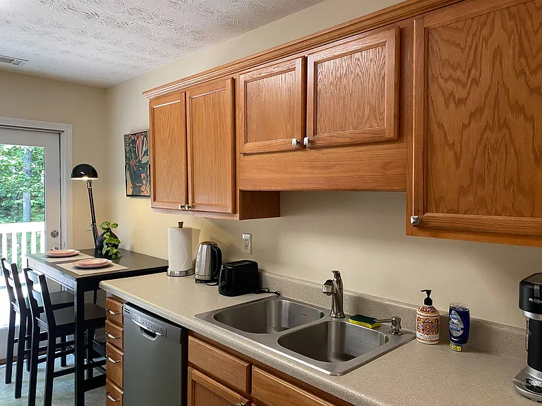 Kitchen with ample wood cabinetry, double-basin sink, dishwasher, and a dining nook by the patio door.