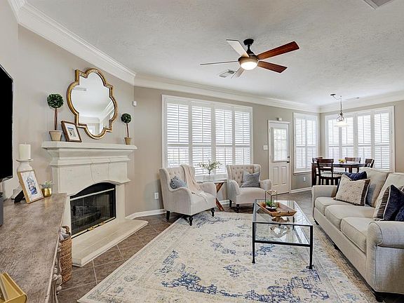 Living room opens into the breakfast nook. Stunning living space with an abundance of natural light, crown molding, plantation shutters, cast stone fireplace, and tile flooring.