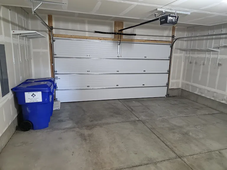 Two-car garage with trash & recycling bins, storage shelving