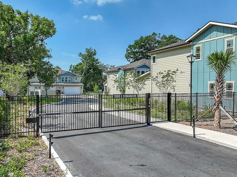 Charming gated community entrance surrounded by lush greenery, featuring modern two-story homes with vibrant exteriors and a welcoming atmosphere.