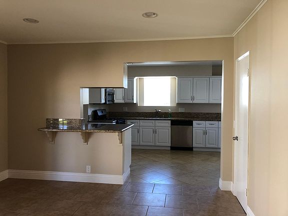 Looking into kitchen from dining room. Breakfast bar with granite countertop to right, sink under garden window just right of stainless steel dishwasher