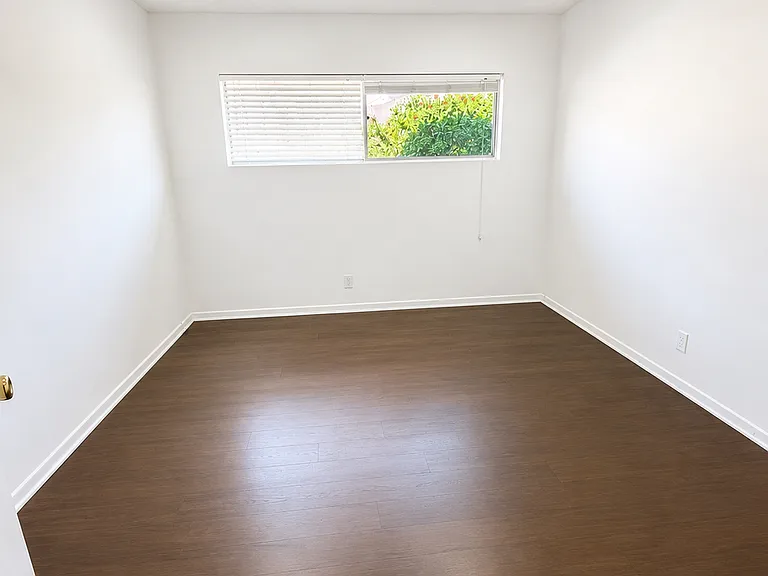 Comfortable bedroom with wood-style flooring, ceiling fan, and natural light.