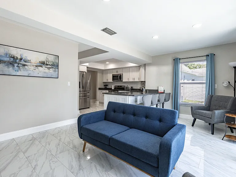 Open living area with lounge seating, large window, and a kitchen with island bar seating and stainless appliances.