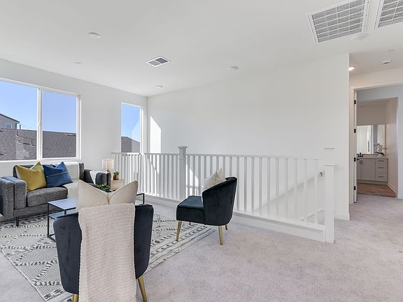 A bright and airy living room with a couch, chairs, and a rug, surrounded by large windows and a bal