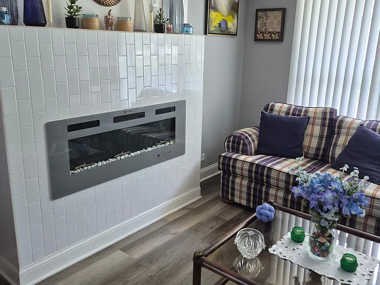 Living room with a tiled accent fireplace, ample seating, and large window blinds providing natural light and privacy.