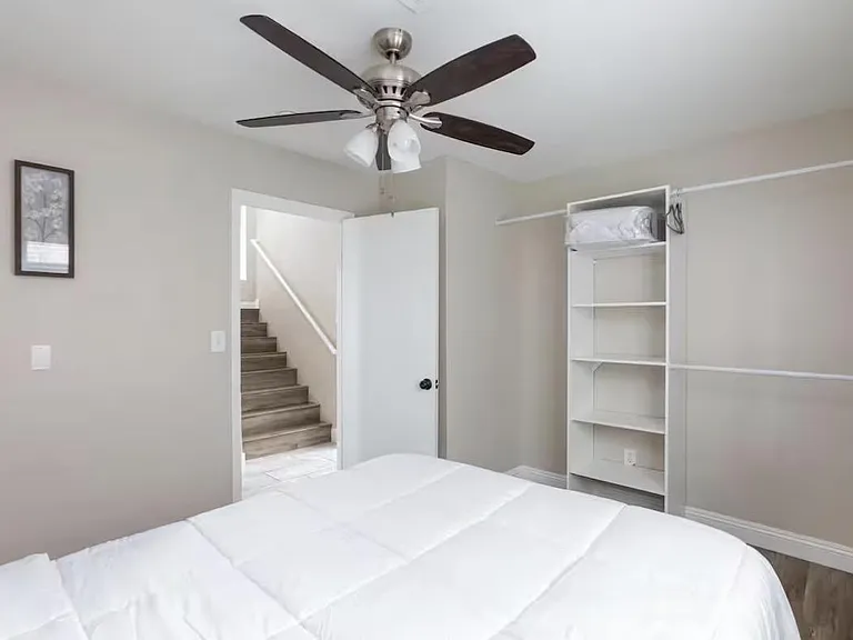 Bedroom features a ceiling fan, neutral walls, and convenient open shelving for linens and personal storage.
