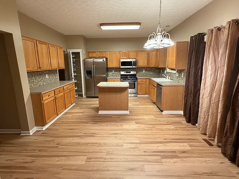 Large open kitchen with natural wood cabinets, center island with storage, pantry. New over the range microwave (2026) and recent refrigerator and washing machine (both 2019). Double glass door to the deck outside.