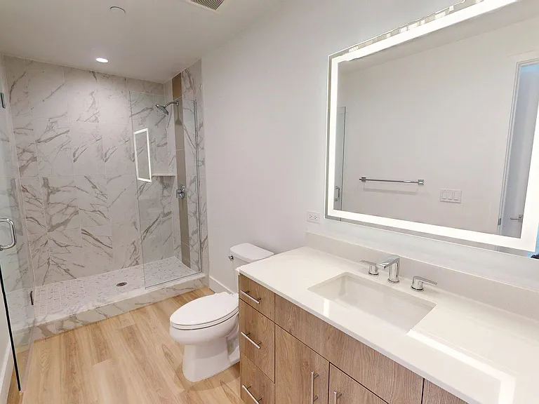 Apartment Bathroom with glass enclosed shower, LED vanity mirror and wood-style floors.