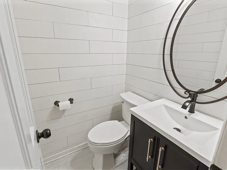 Modern powder room with white subway tile walls, dark vanity, round mirror, and oil-rubbed bronze fixtures.