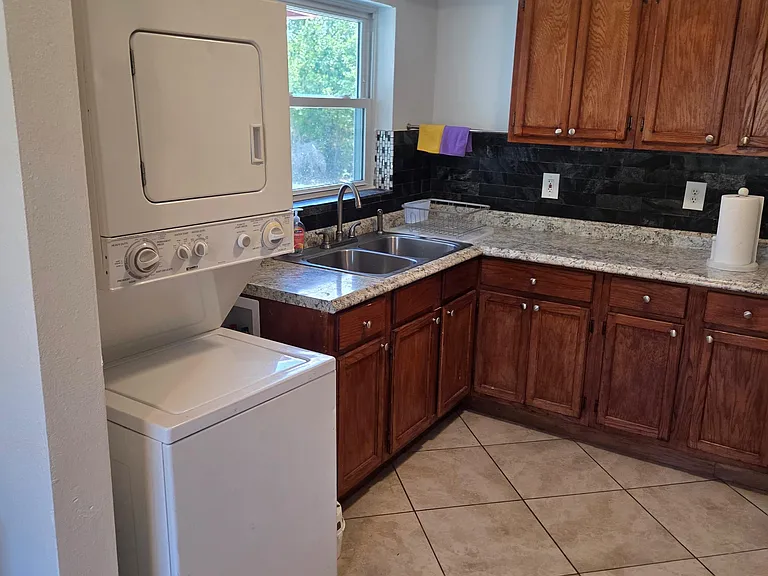 Functional kitchen with ample wood cabinetry, double-basin sink, tile flooring, and convenient in-unit stacked laundry.