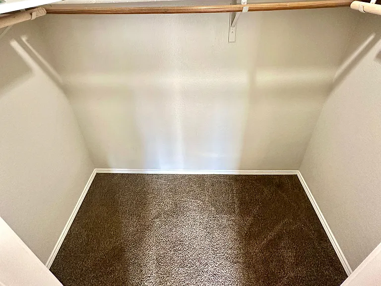 Walk-in closet with carpet flooring, a full-length hanging rod, and an upper shelf for organized storage.