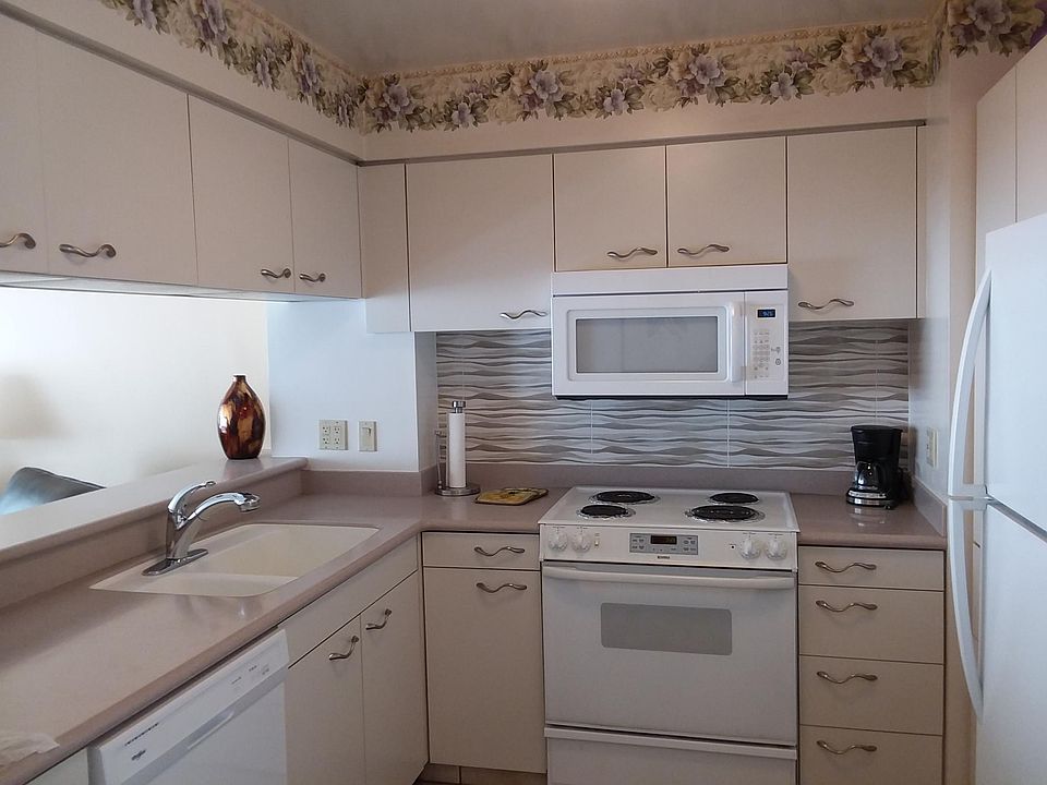 Kitchen with new refrigerator, dishwasher, above stove microwave. Corian counter top. Designer Italian Tile, wave handles accent all cabinet doors.
