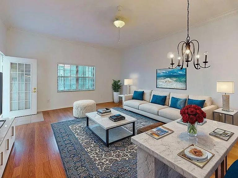 Elegant living room with stylish decor, featuring a cozy white sofa with blue cushions, a chic chandelier, and a marble coffee table adorned with red roses, creating a welcoming atmosphere.