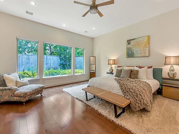 The expansive Primary Bedroom features rich wood floors, large portrait windows, and enhanced custom lighting.