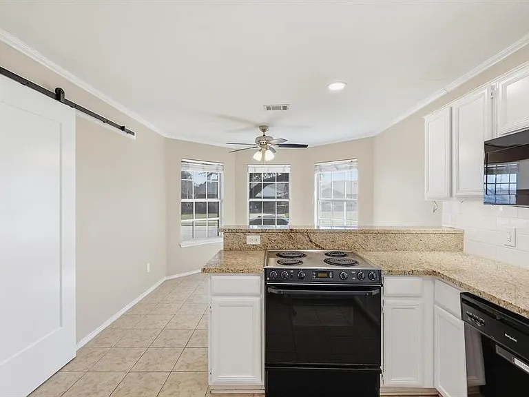 Kitchen featuring a peninsula, a barn door, black appliances, white cabinetry, and a ceiling fan