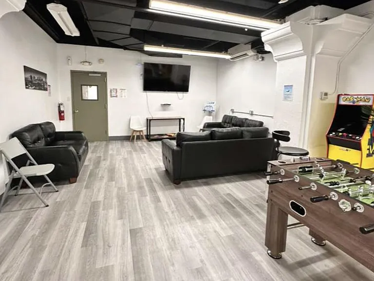 Spacious shared lounge with sectional seating, wall-mounted TV, and game area featuring foosball and an arcade cabinet.