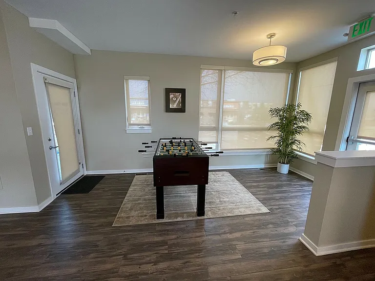Bright apartment corner with elegant laminate flooring, featuring a foosball table and stylish decor accentuated by natural light and a potted plant.